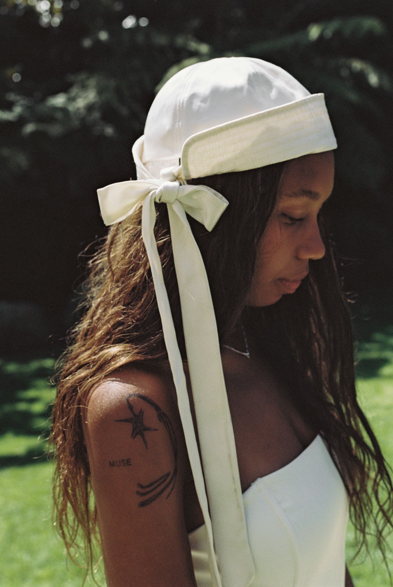 Woman with long hair wearing a white satin bonnet with ribbon bow, showing a star tattoo on her shoulder.