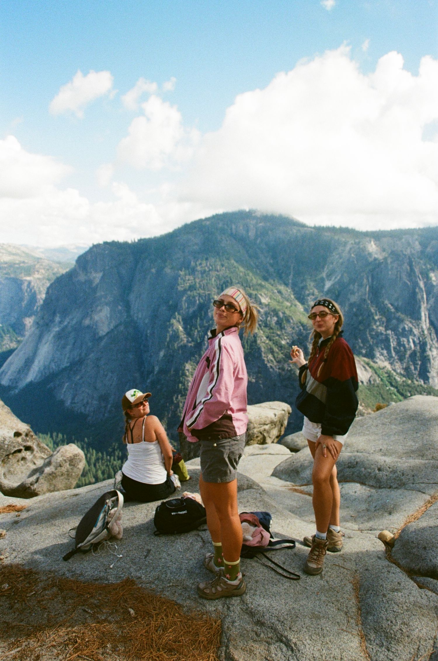 Three hikers stand on a rocky summit in Yosemite National Park with stunning mountain valley views.