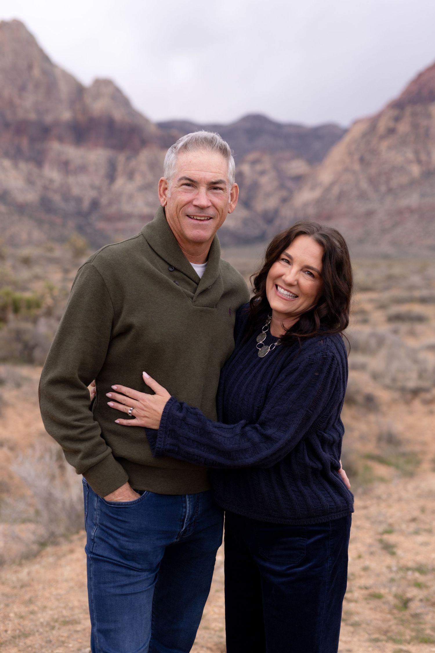 Smiling couple embracing outdoors at Red Rock Canyon, man in green sweater and woman in navy top.