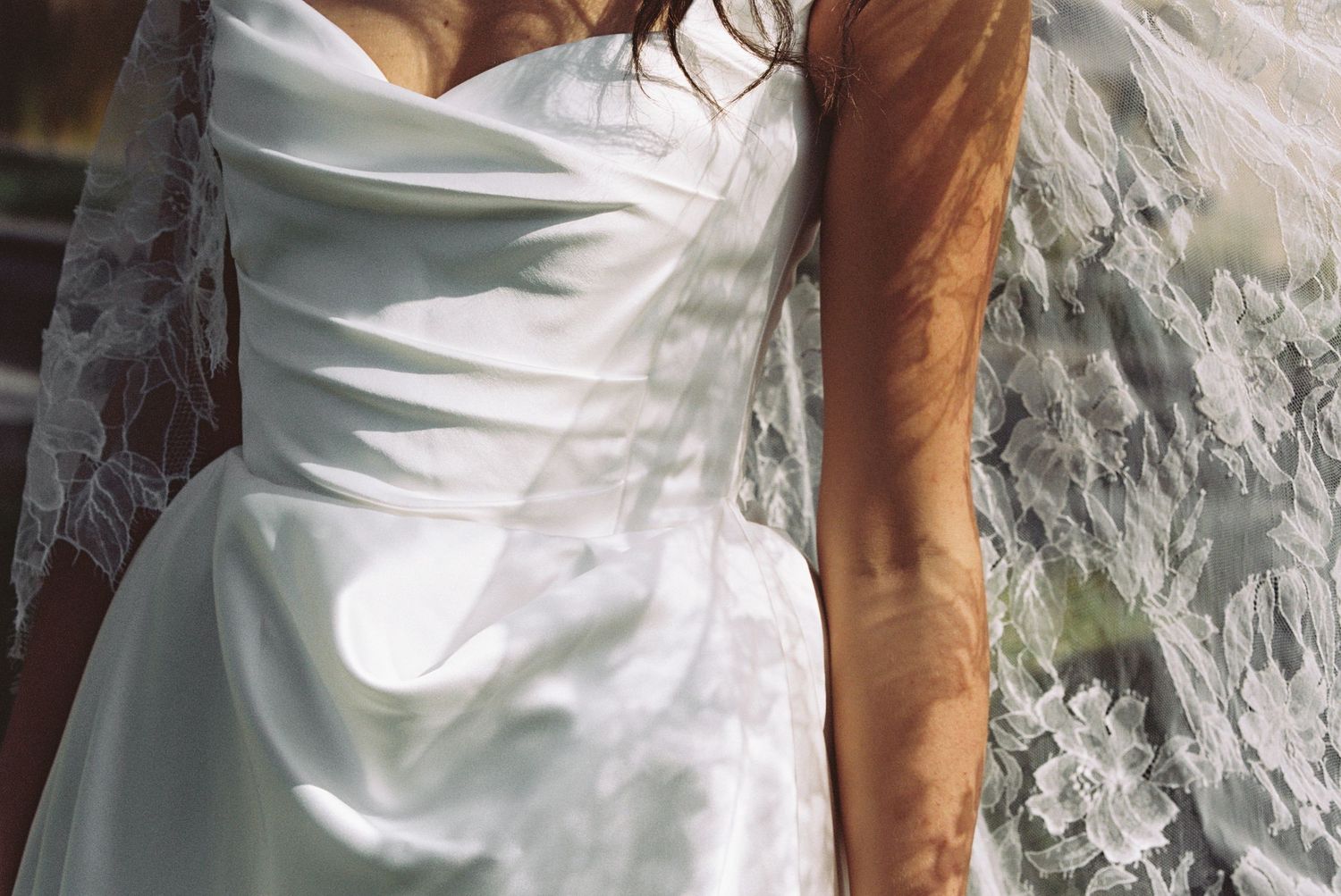 Close-up of a bride in a white strapless satin wedding dress with lace veil detail.