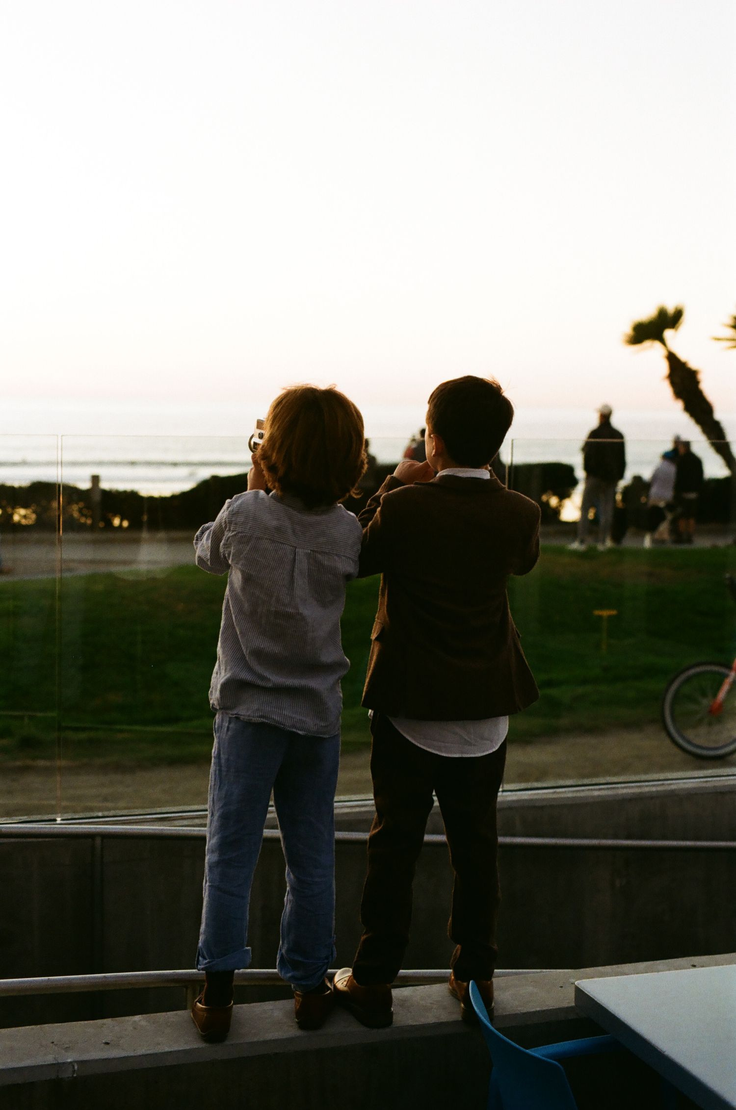 Two children standing on ledge watching sunset over ocean at outdoor wedding reception venue.