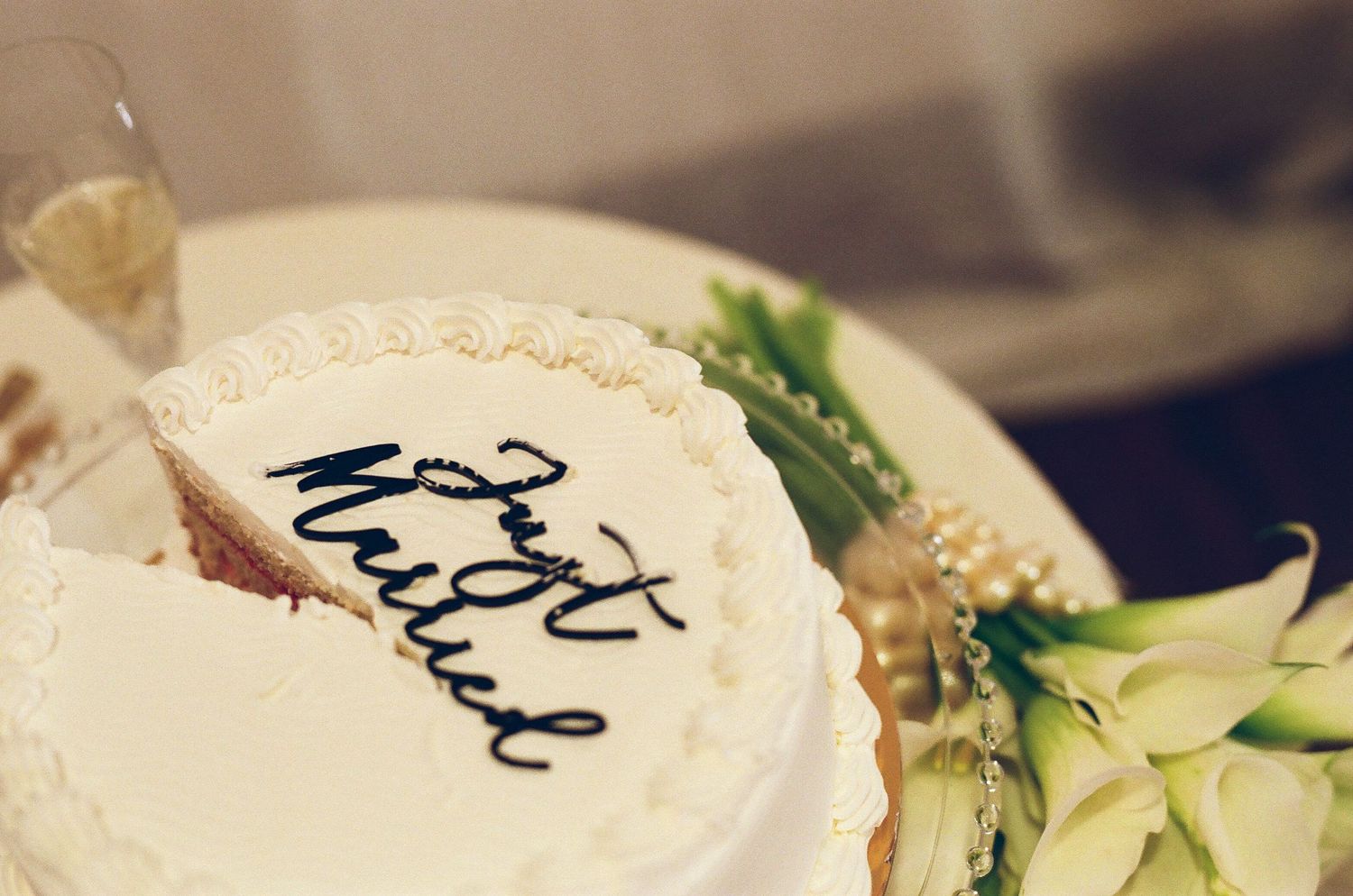 White wedding cake decorated with black script reading Just Married beside calla lily bouquet.