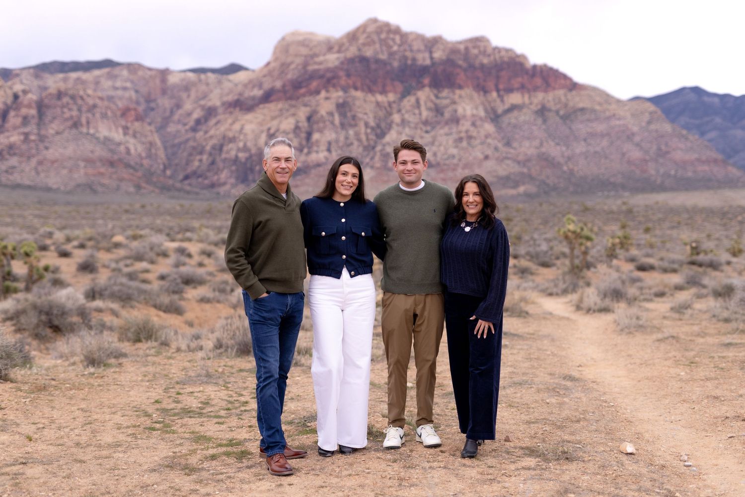 Four people smiling together on a desert trail with red rock mountains in the background at Red Rock Canyon.