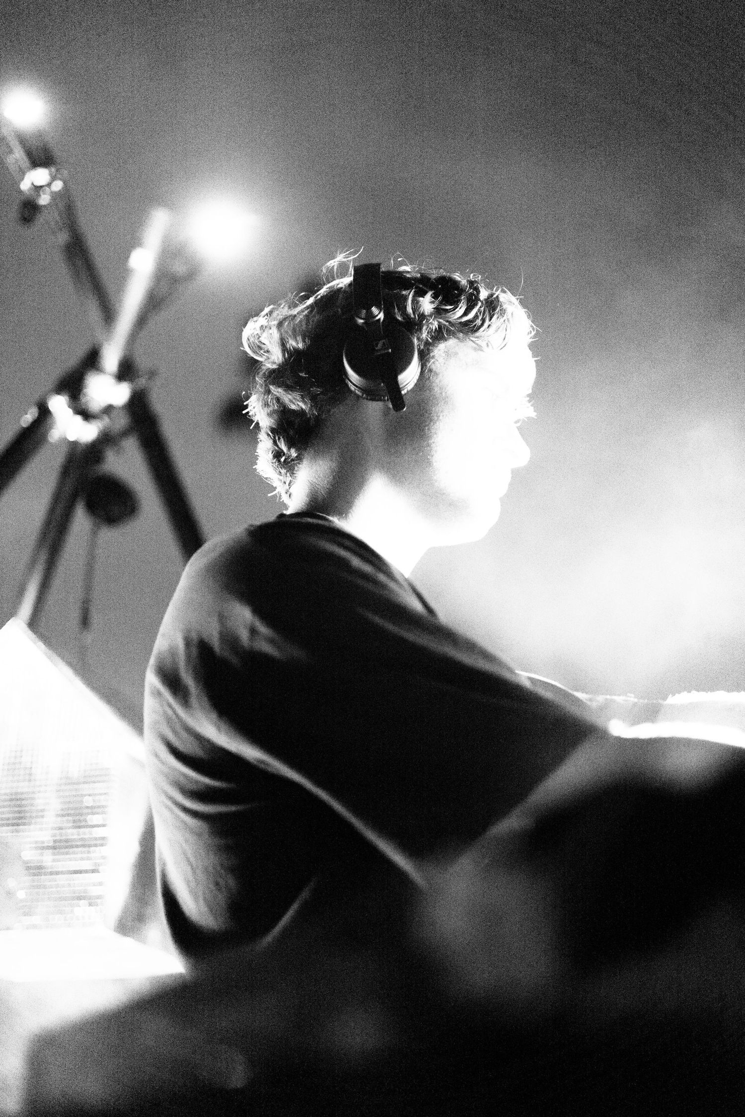 Black and white profile of DJ wearing headphones performing on stage under bright lights.
