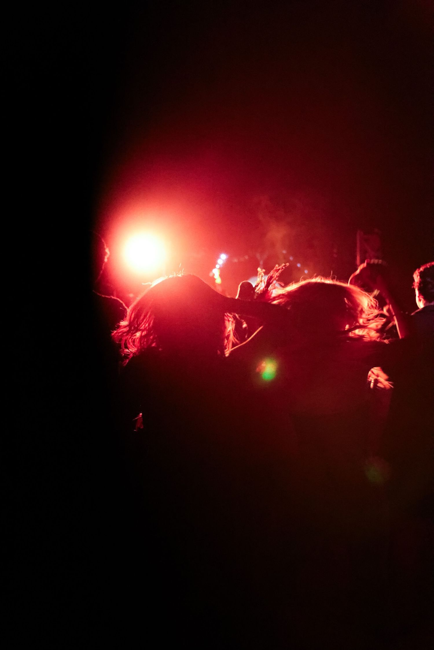 Silhouettes of concert crowd under dramatic red stage lighting in a dark venue.