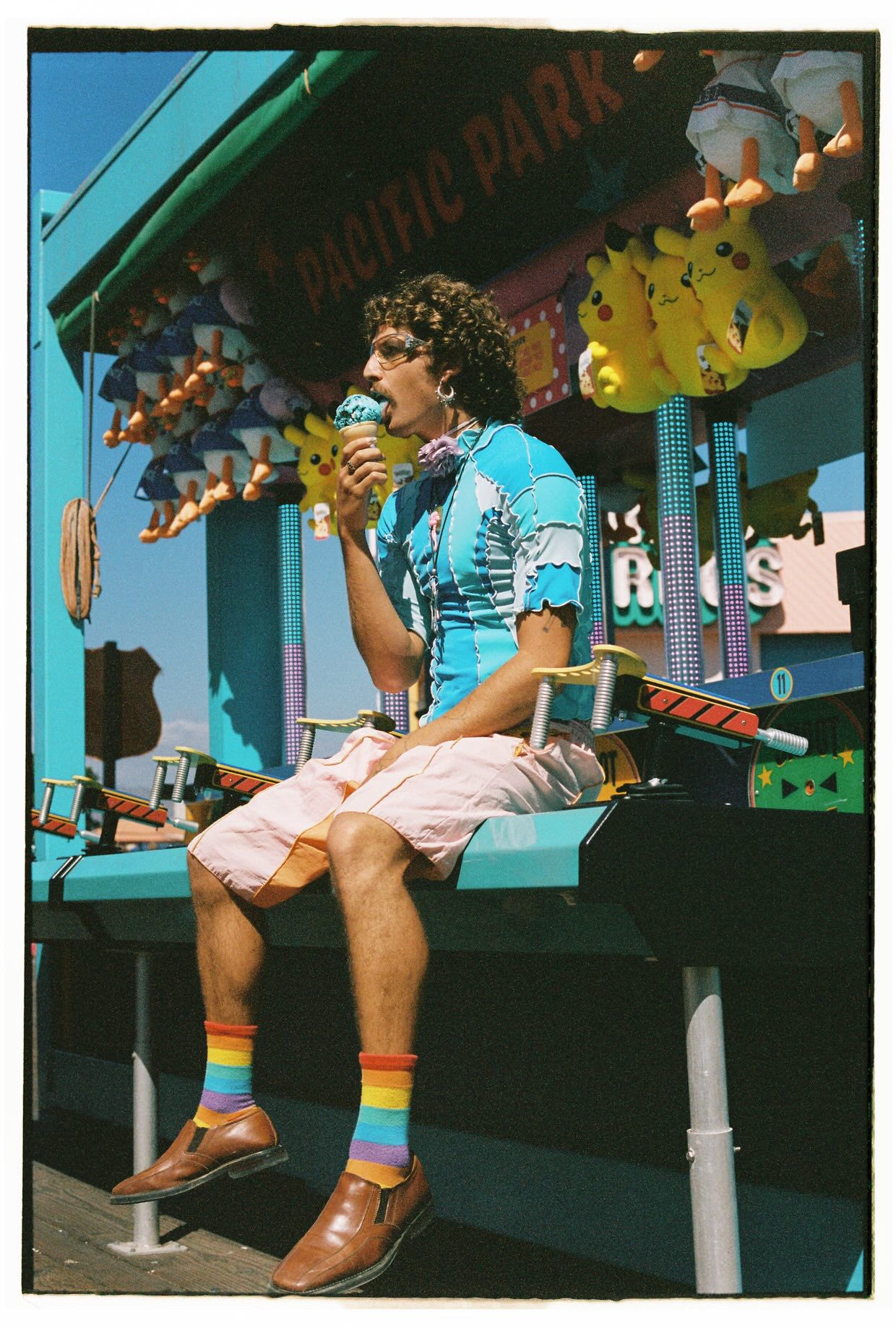 Person in blue shirt eating ice cream cone seated outside Pacific Park amusement venue.