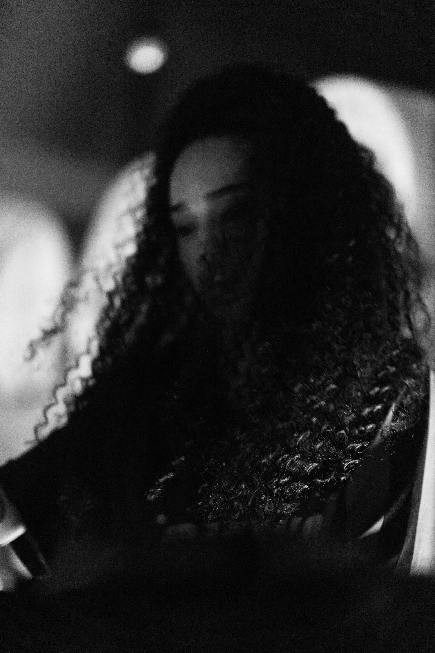 Black and white portrait of a woman with curly hair in a dark atmospheric setting.