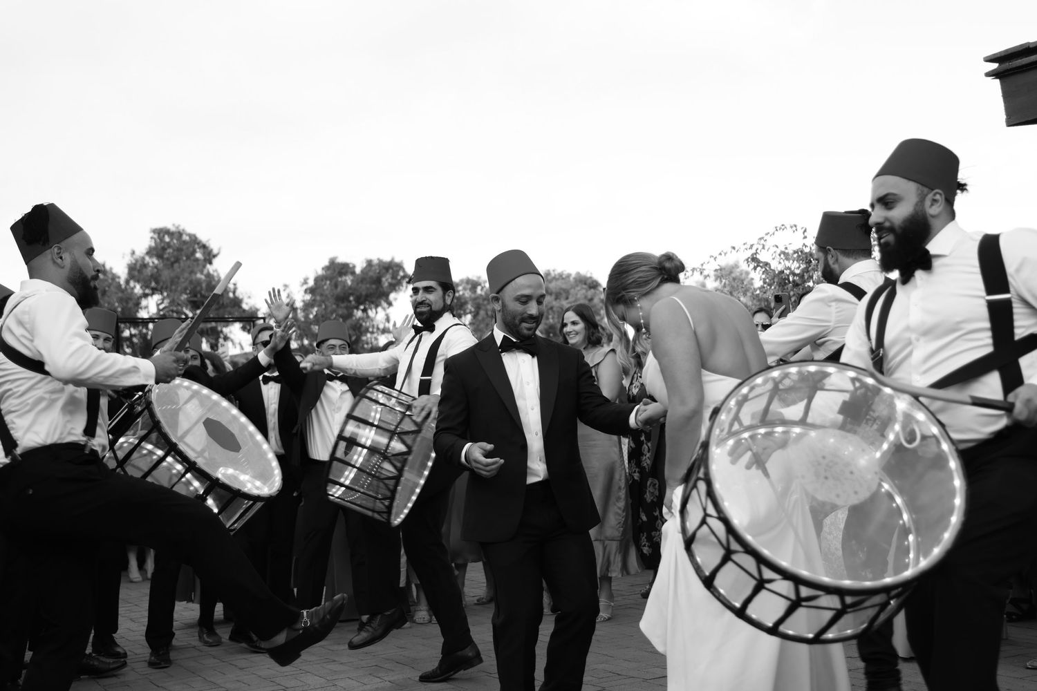 Groom celebrates with traditional drummers in fez hats during lively wedding procession.