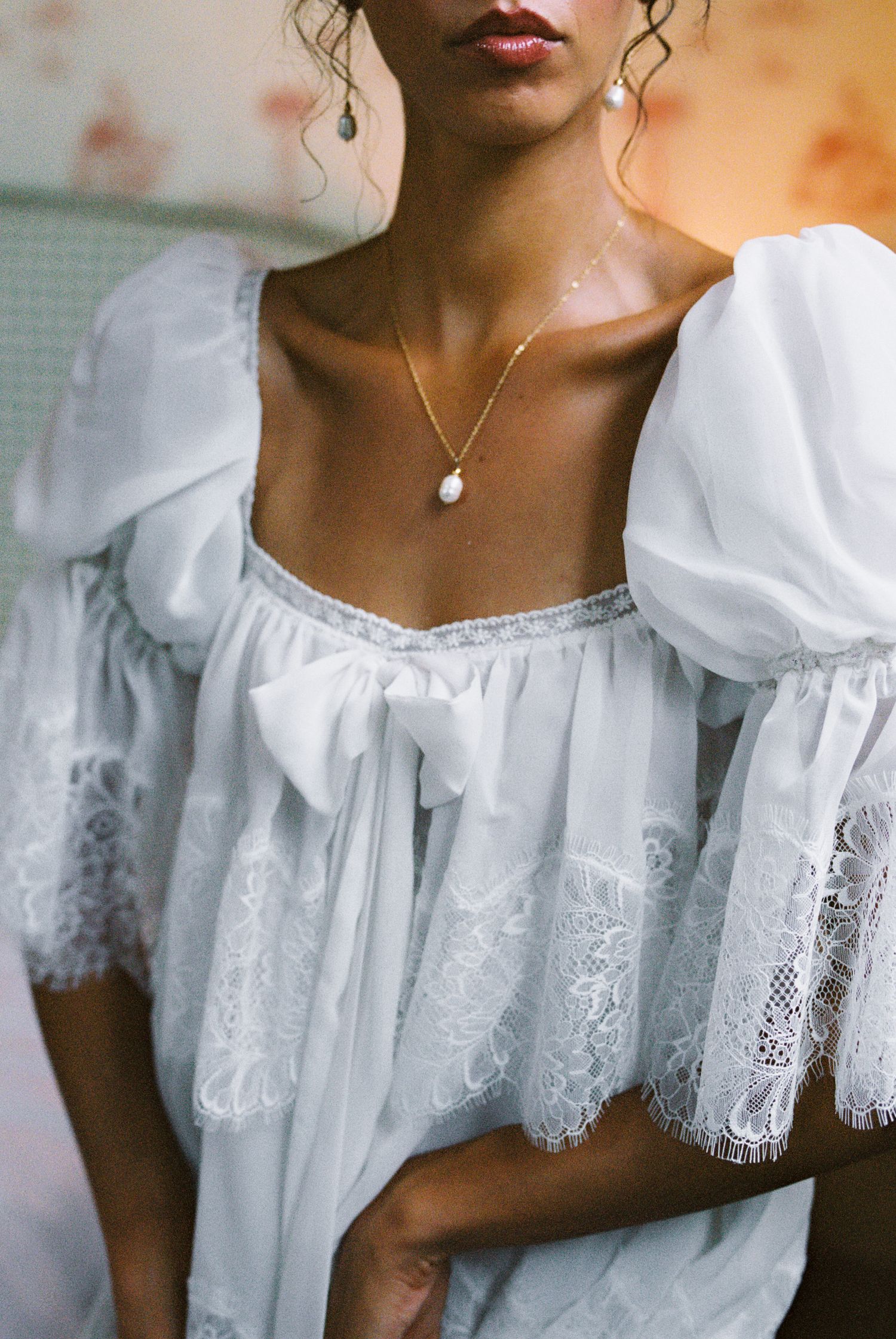 Woman in white lace puff-sleeve dress with bow detail, wearing a pearl drop necklace and pearl earrings.