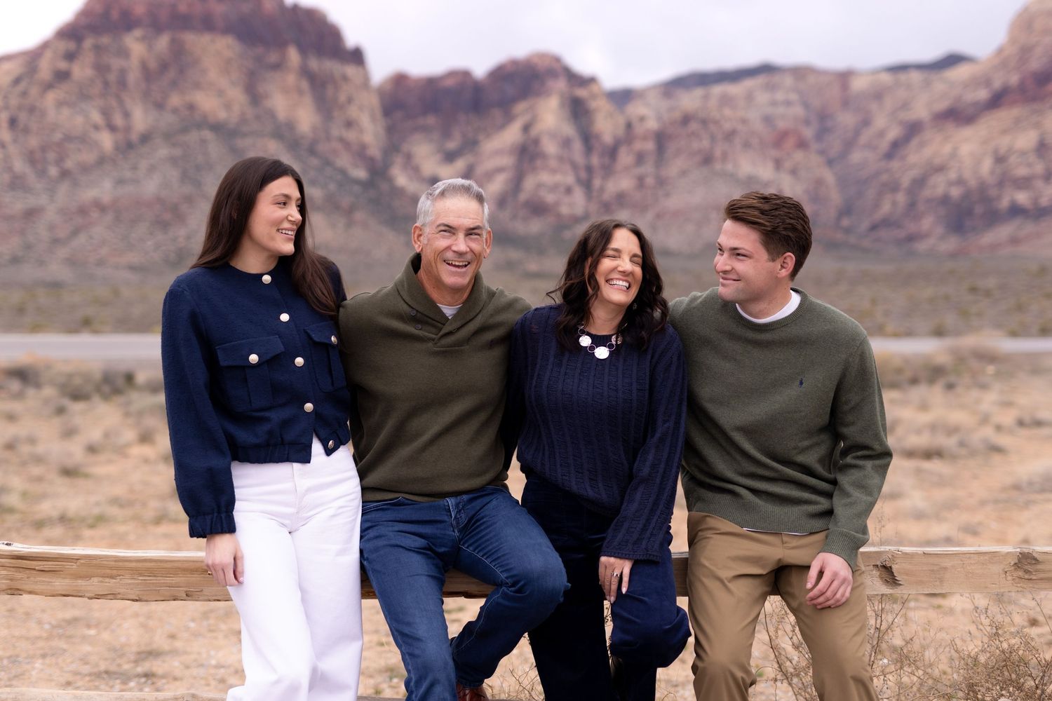 Family of four smiling outdoors at Red Rock Canyon, Nevada, with scenic red rock formations in the background.