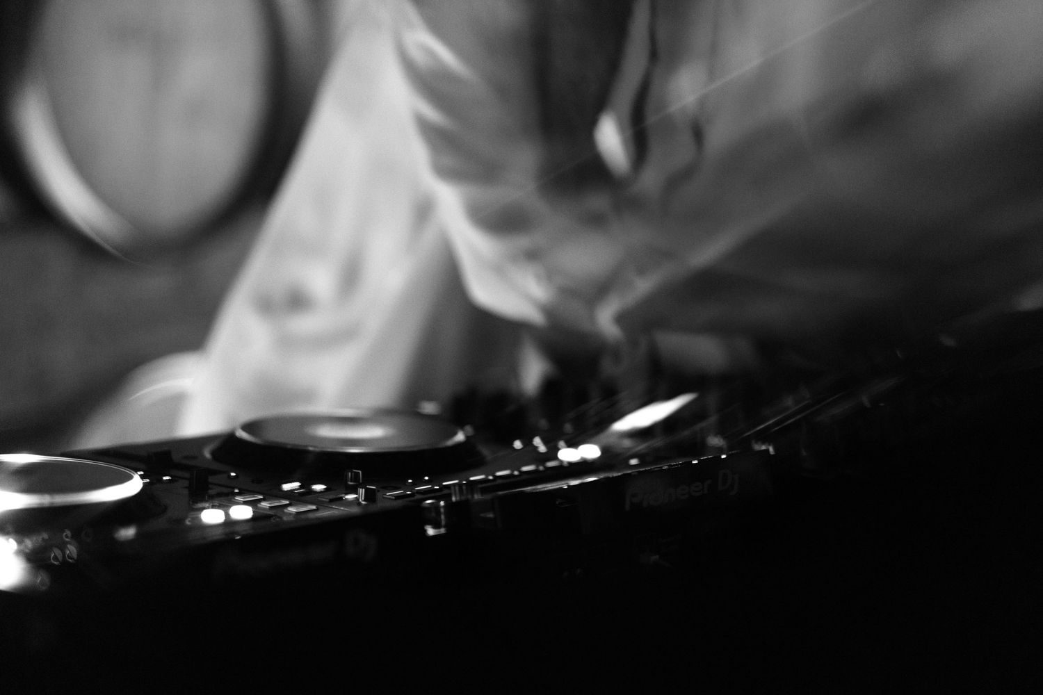 Monochrome photo of DJ equipment with blurred hands mixing tracks at a nightclub event.