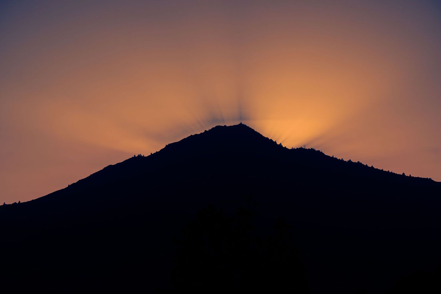 Dramatic silhouette of a mountain peak with sunburst rays radiating at golden sunset.