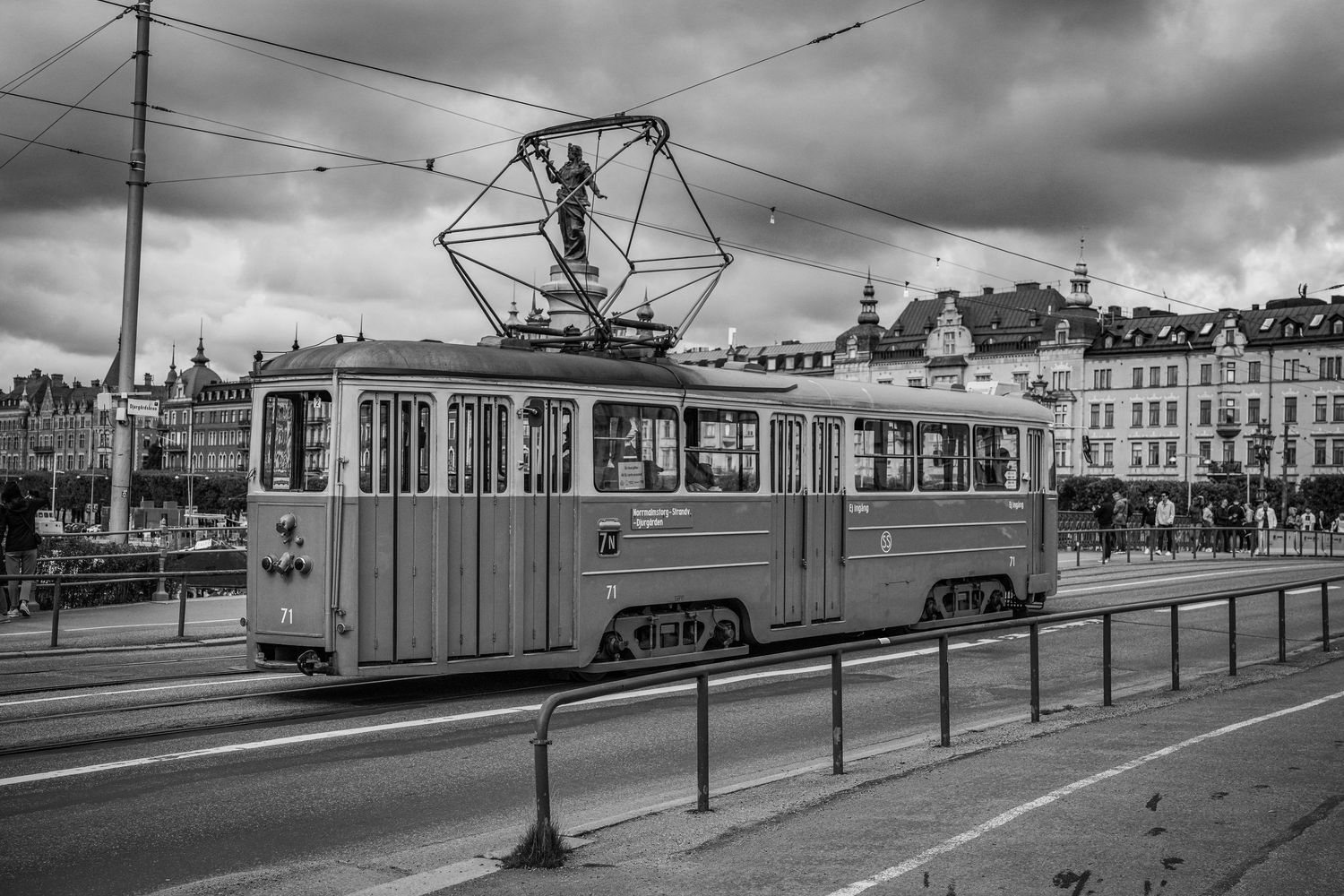 Black and white photo of a vintage tram on a city bridge with historic buildings in the background.