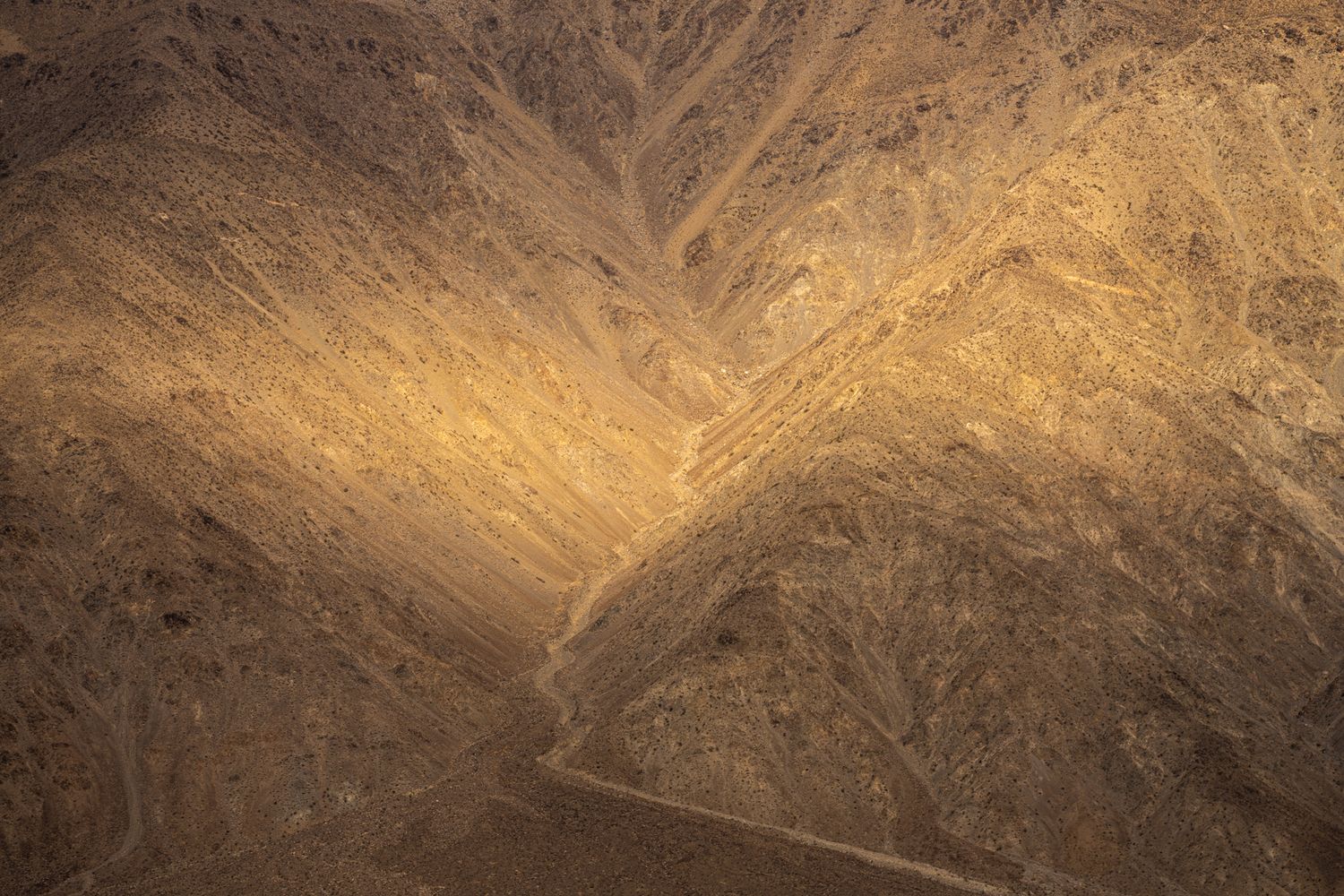 Aerial view of eroded desert mountain terrain with deep ravines and a winding road below.