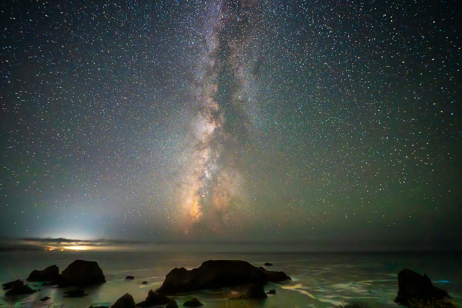 Milky Way galaxy rising over rocky Pacific coastline under a stunning star-filled night sky.