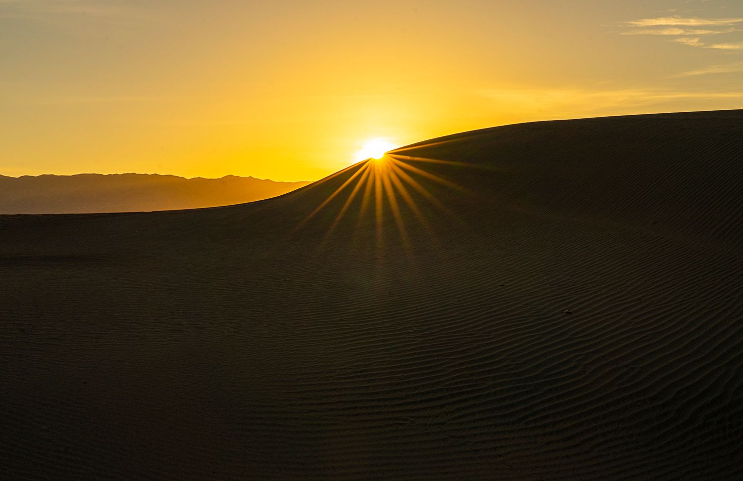Stunning sunburst over rippled sand dune at golden sunset in desert landscape.