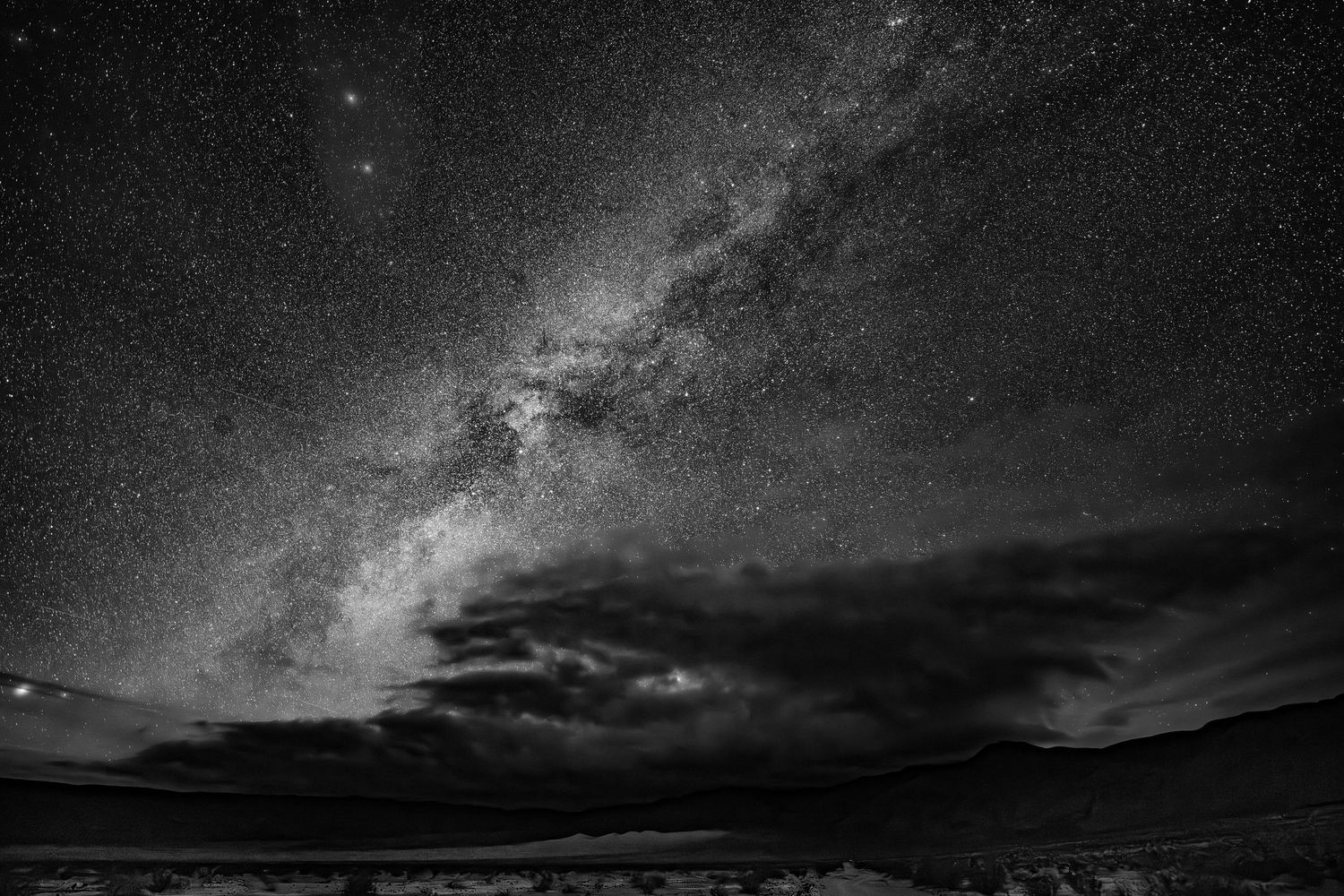 Stunning black and white Milky Way galaxy over a dark desert landscape with dramatic clouds.