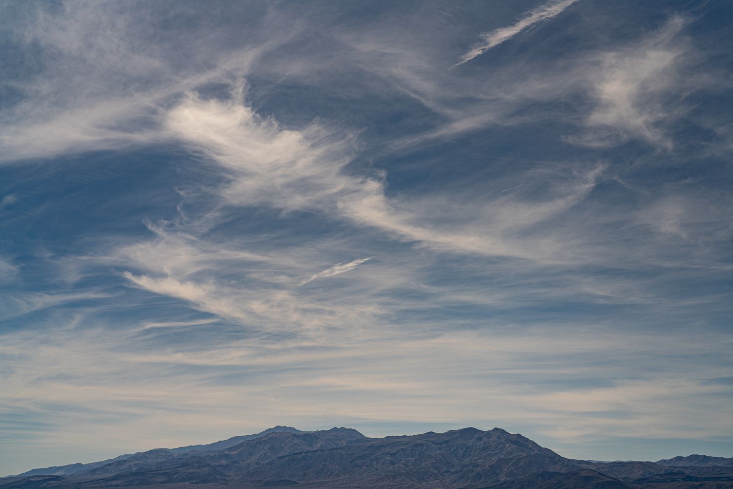 Wispy cirrus clouds streaking across a vivid blue sky above distant mountain silhouettes.