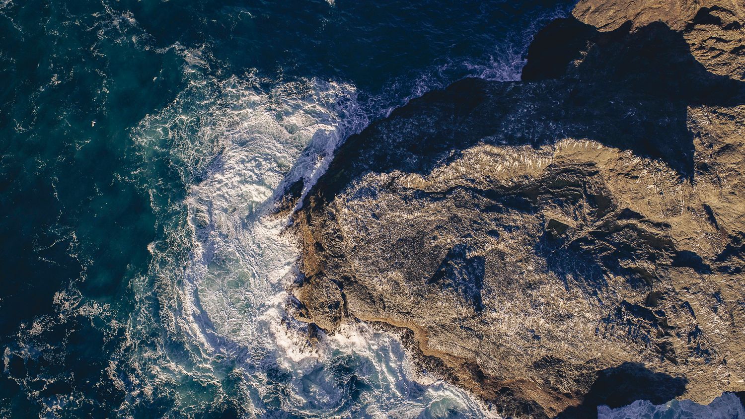 Aerial top-down view of ocean waves crashing against rugged rocky coastal formations.