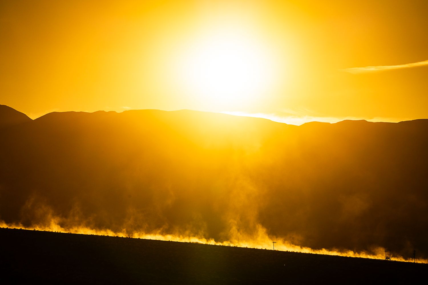 Golden sunset silhouettes mountain ridges with misty haze rising from desert floor.