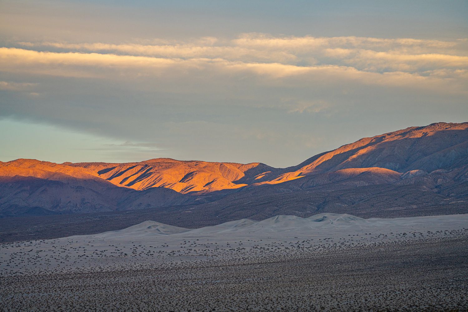 Golden sunset light illuminating dramatic mountain ridges over a vast desert valley landscape.