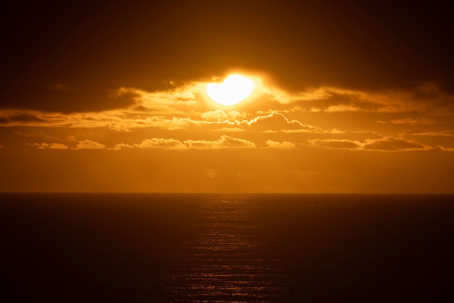 Golden sunset over calm ocean with dramatic clouds and glowing orange sky.