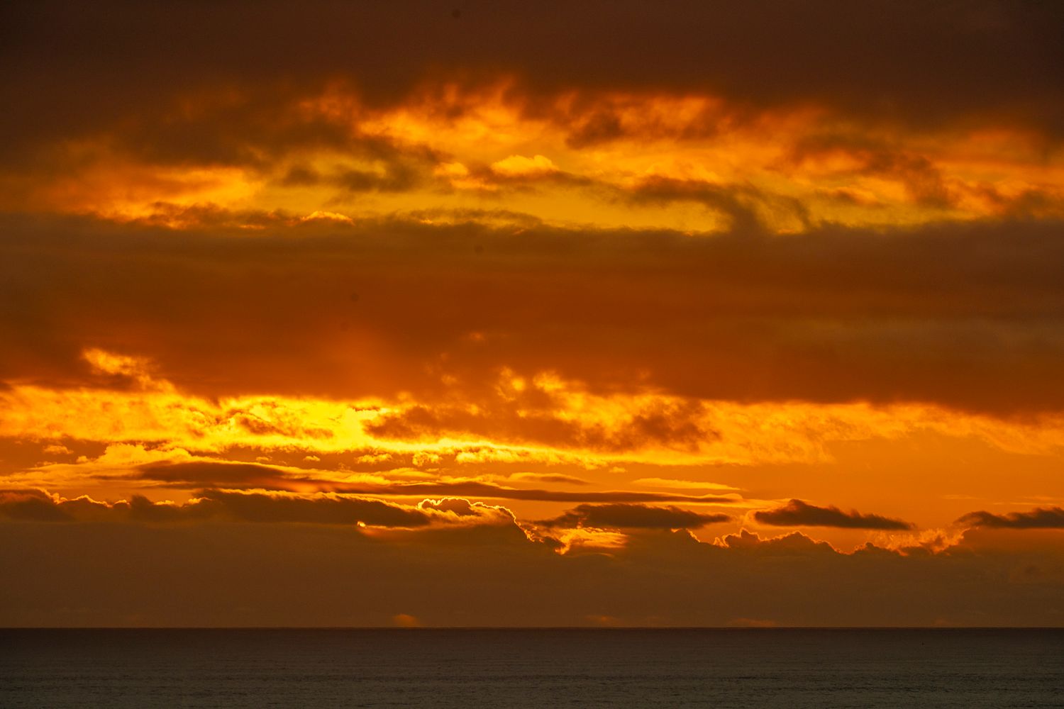 Vivid orange and red sunset sky with layered dramatic clouds over dark ocean horizon.