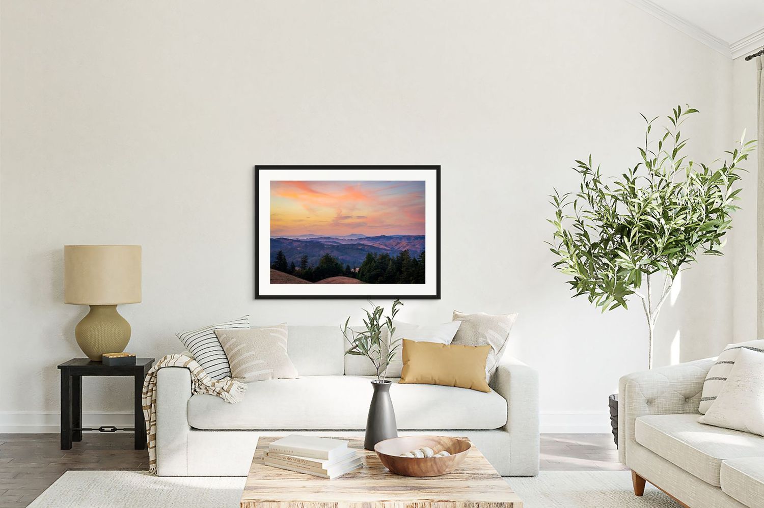 Framed landscape painting of a vibrant mountain sunset displayed above a white sofa in a modern living room.