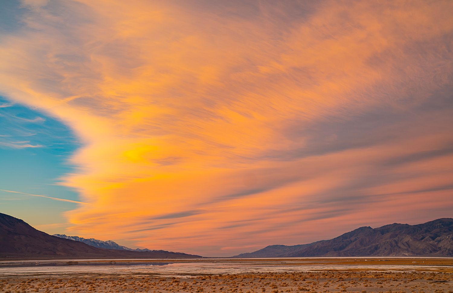 Dramatic orange lenticular clouds over vast desert valley with distant mountain range at sunset.