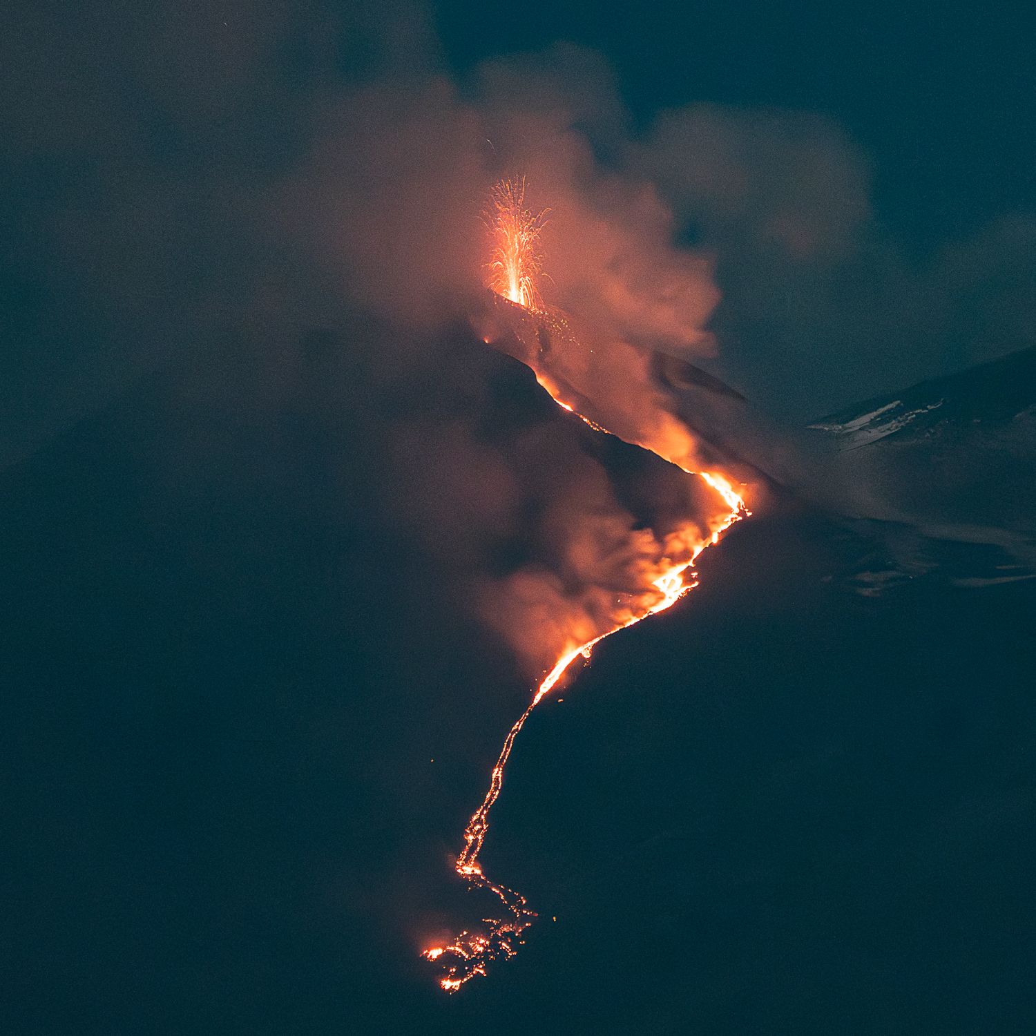 Mount Etna volcanic eruption at night showing bright orange lava streams flowing down dark slopes.