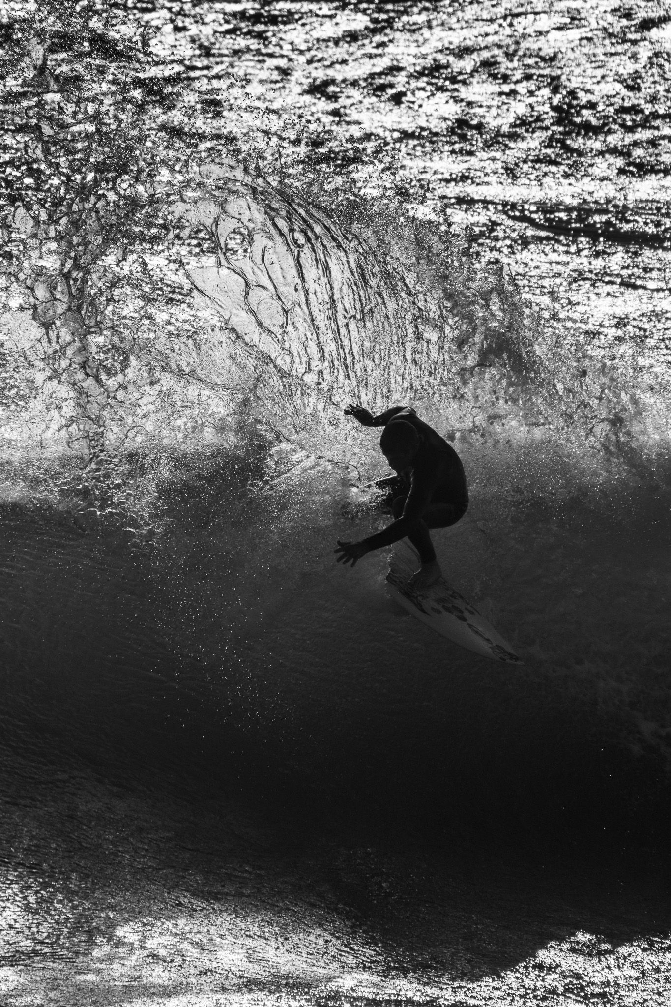 Black and white dramatic silhouette of a surfer riding inside a massive breaking ocean wave.