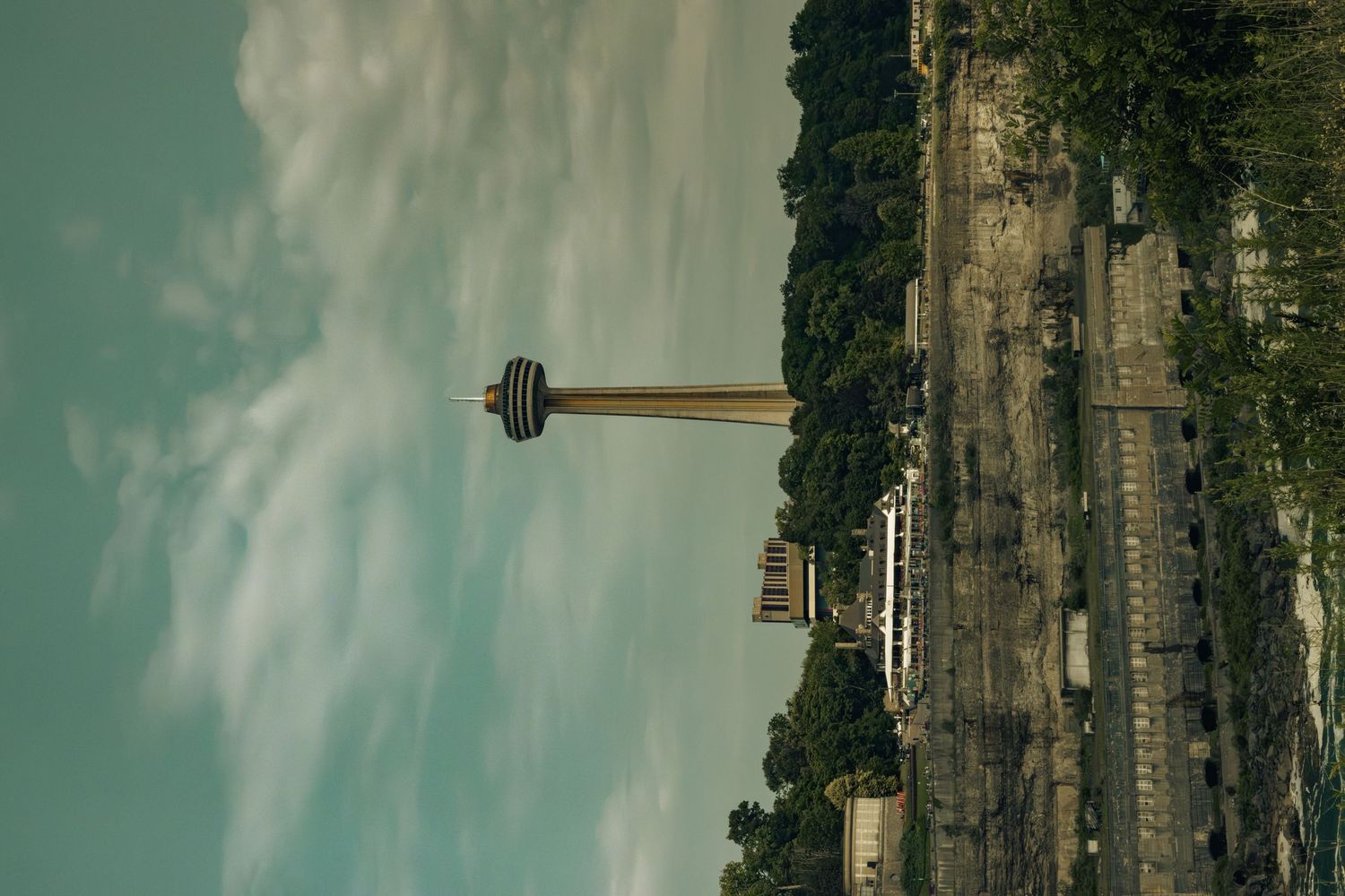 Tall observation tower rising above lush green trees beside a river under a cloudy sky.