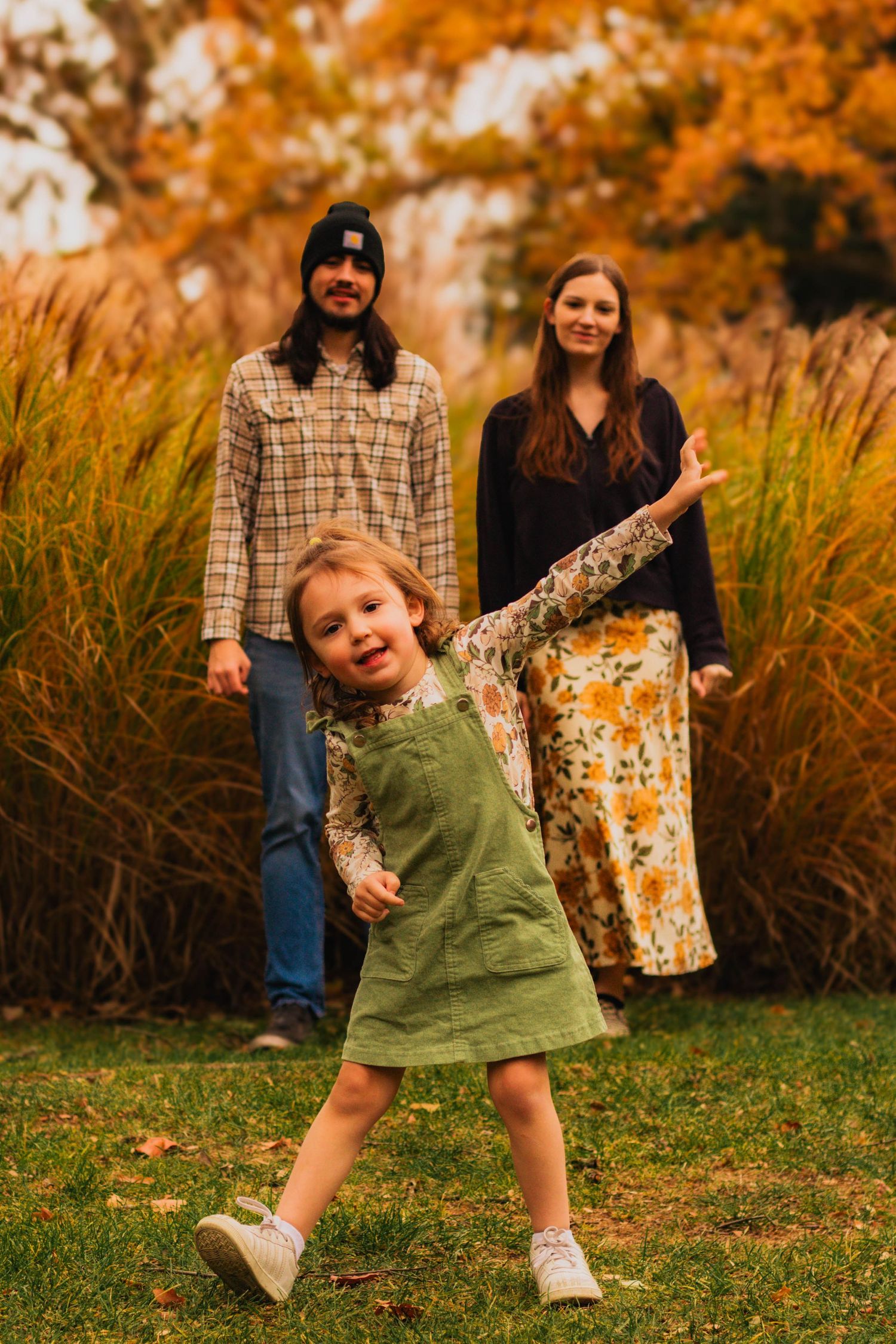 A playful autumn family photo with a child dancing in a green dress against fall foliage.
