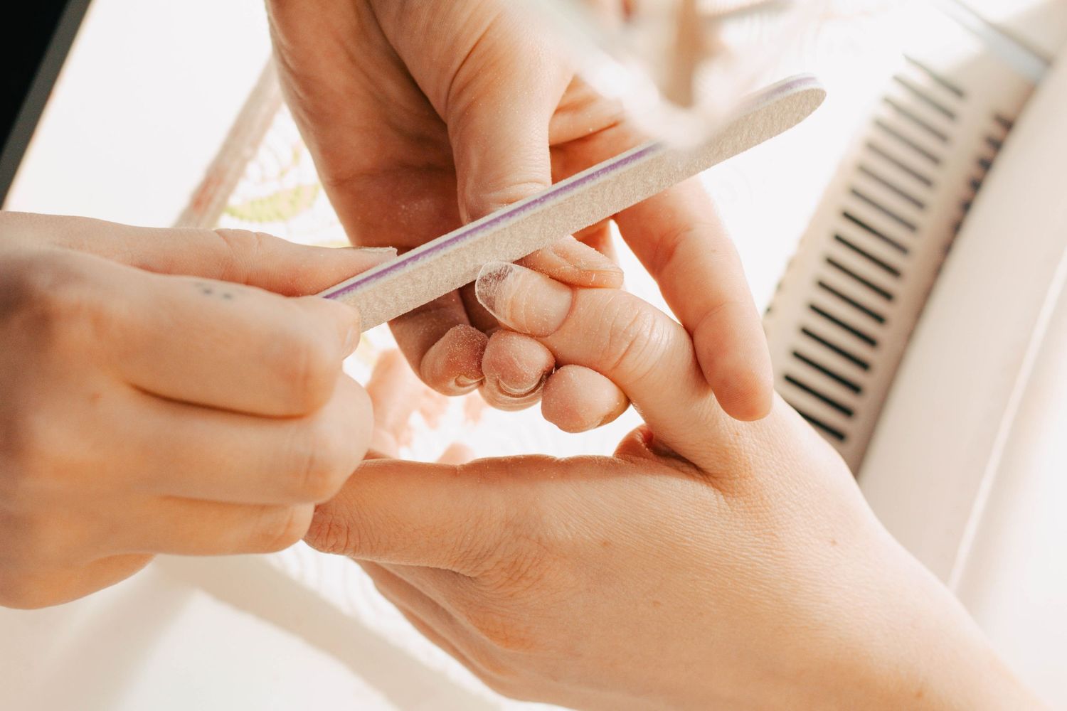 Close-up of hands performing a professional manicure treatment with nail file in bright natural lighting.