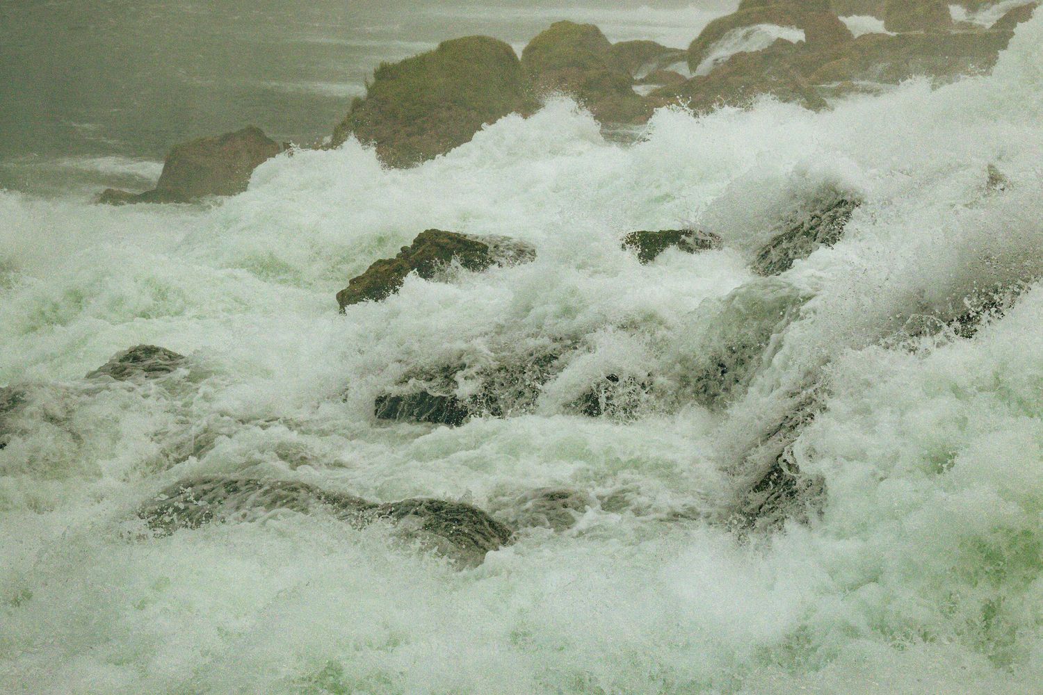 Turbulent white water rapids rushing over moss-covered rocks in a powerful river current.