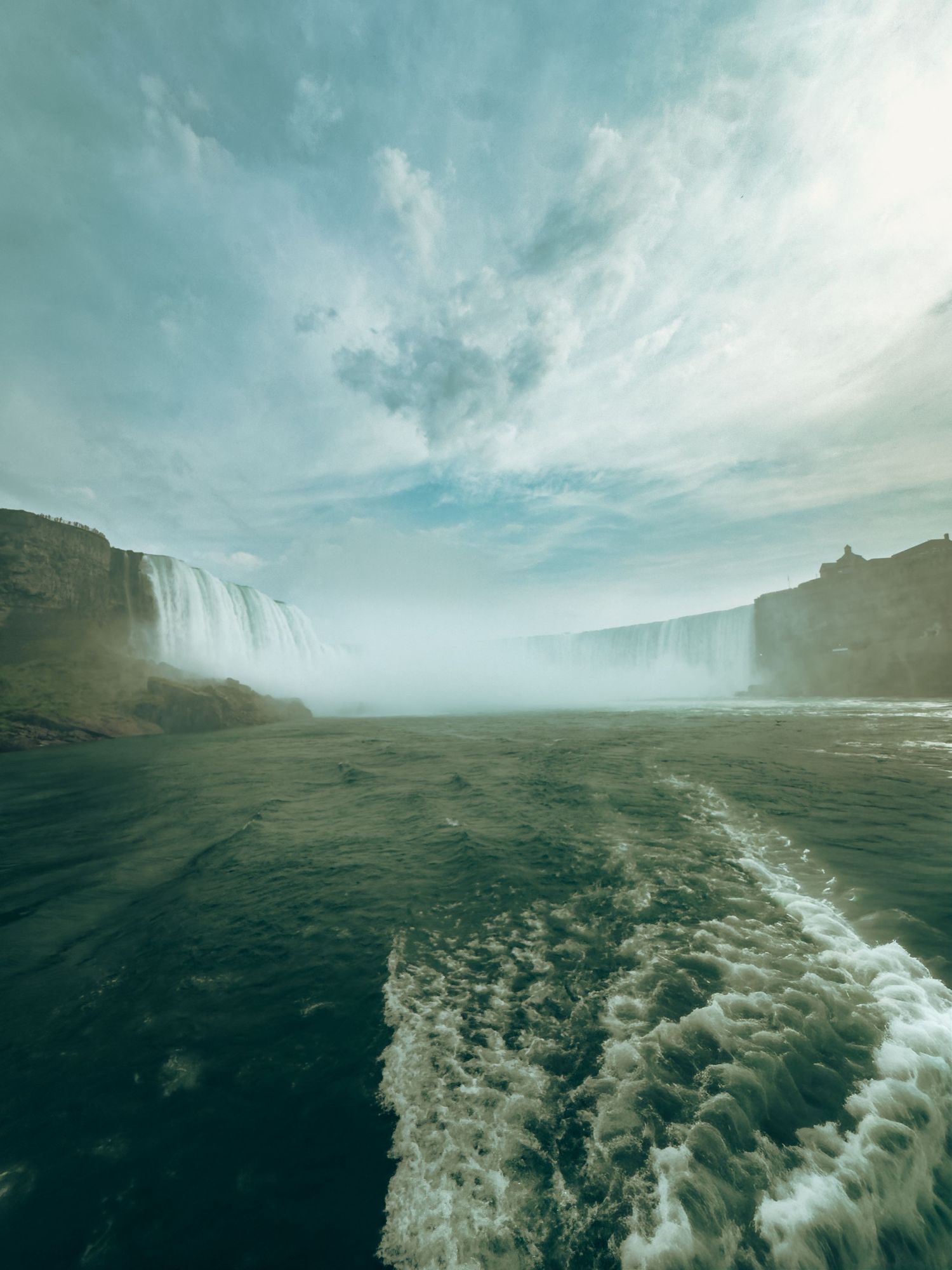 A powerful waterfall cascades into a misty river gorge under a dramatic cloudy sky.
