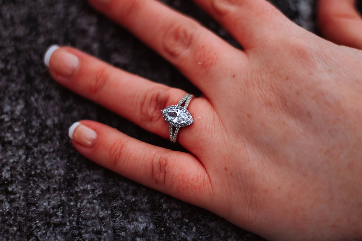 Close-up shot of sparkling diamond ring on hand against dark surface.
