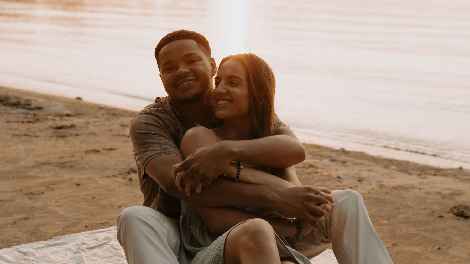 A happy couple embraces on a sandy beach at sunset, sharing a warm and romantic moment together.