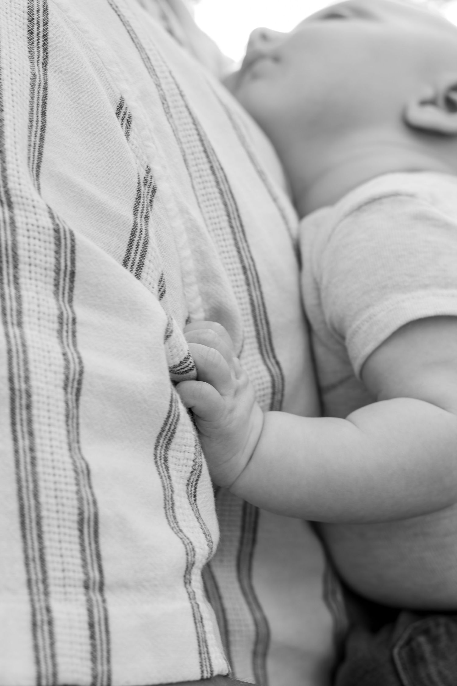 Black and white photo of a baby resting on an adult's chest, tiny hand gripping their striped shirt.
