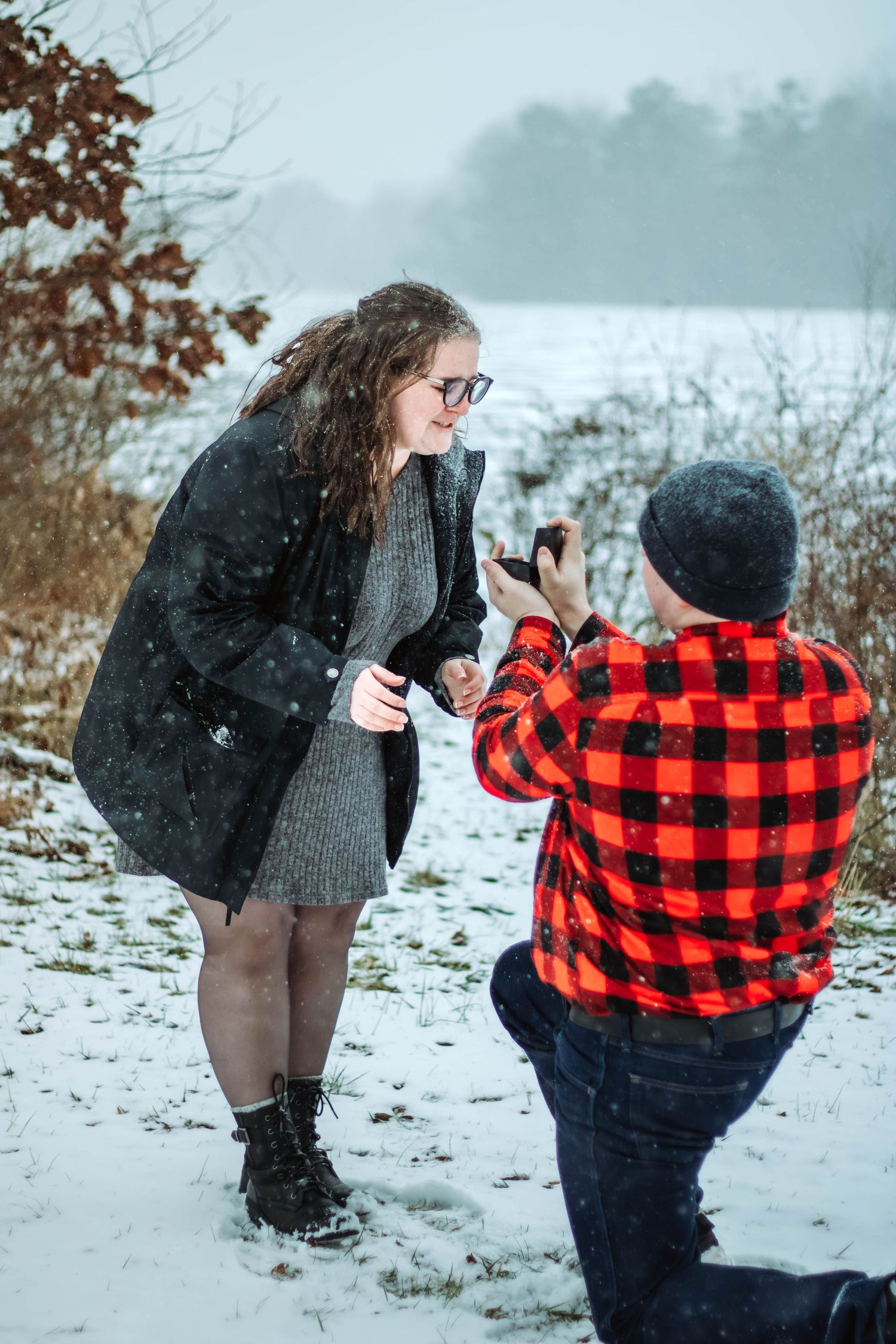 A winter proposal scene with one person kneeling in red plaid while the other stands in a black coat.