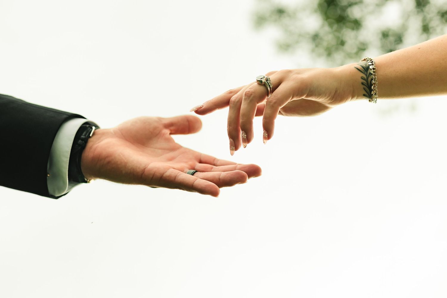 Two hands reaching toward each other, one wearing a ring and bracelet, symbolizing love and connection.