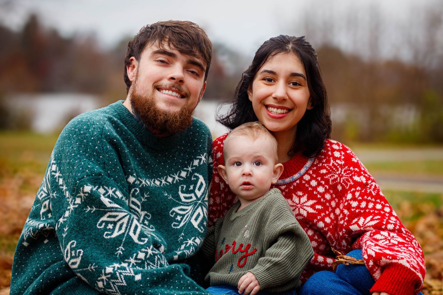 Family of three poses together wearing matching winter sweaters with snowflake patterns.
