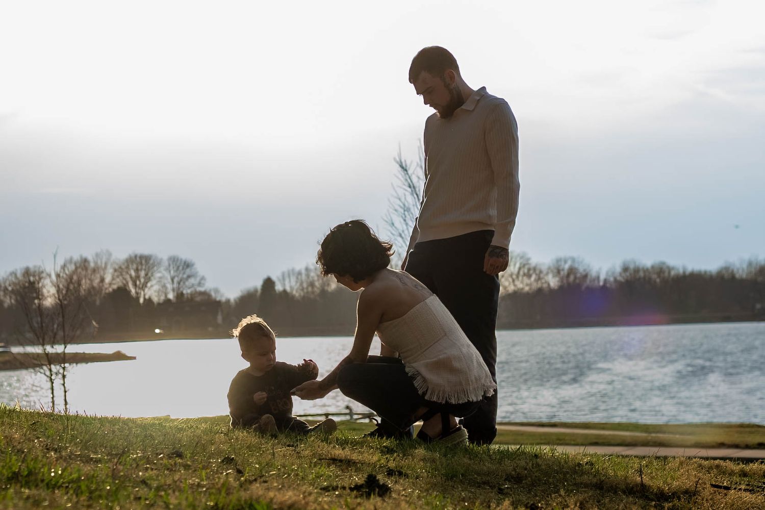 A series of silhouetted figures sit peacefully by a tranquil lake during sunset, creating a serene outdoor scene.