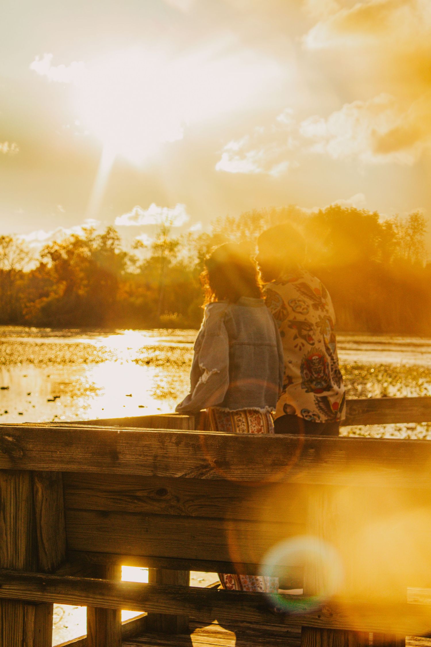 Silhouetted figures sit on a dock during a dramatic golden sunset over water.