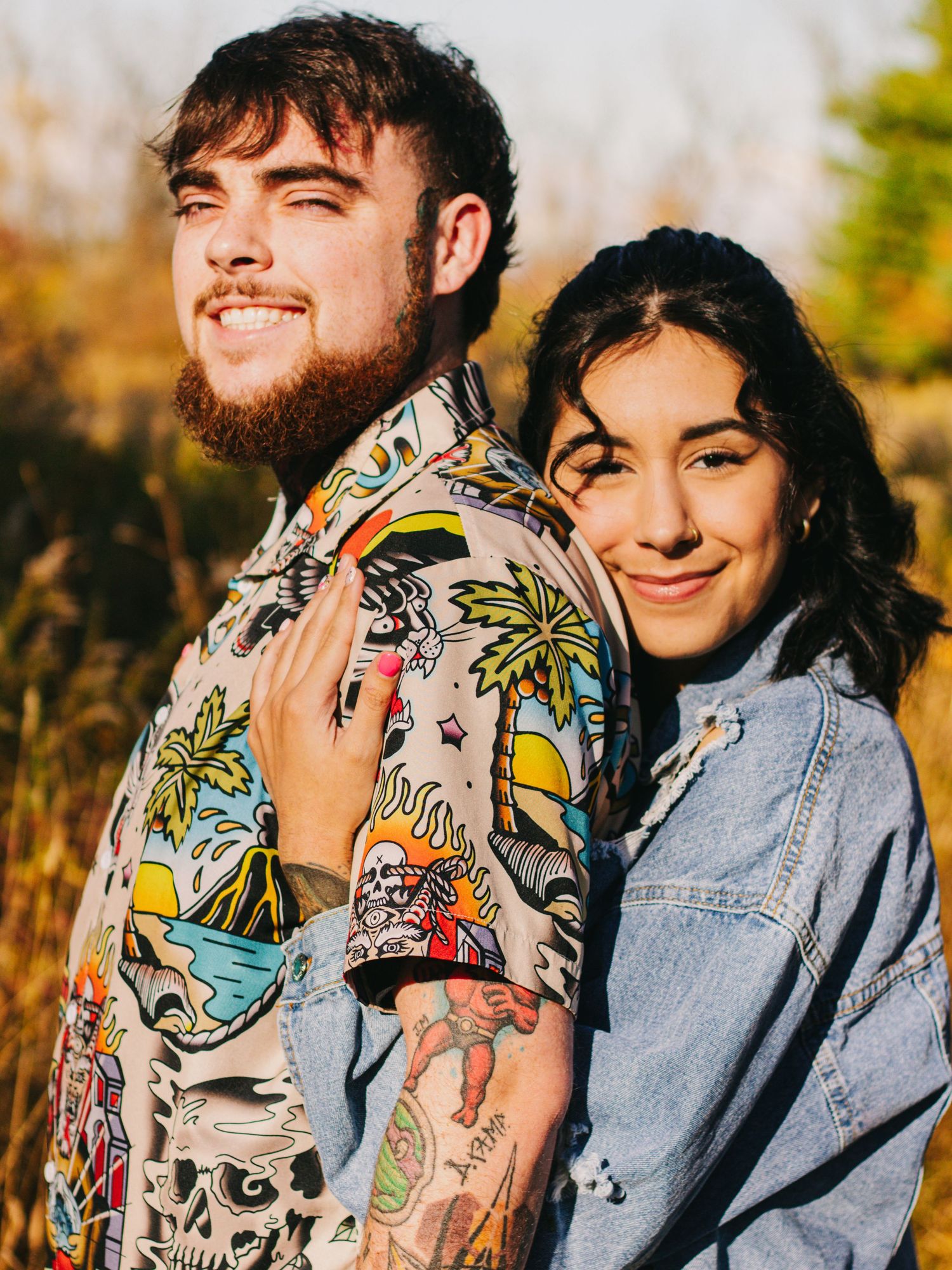 A couple embraces outdoors wearing denim and a tropical print shirt during an autumn photoshoot.