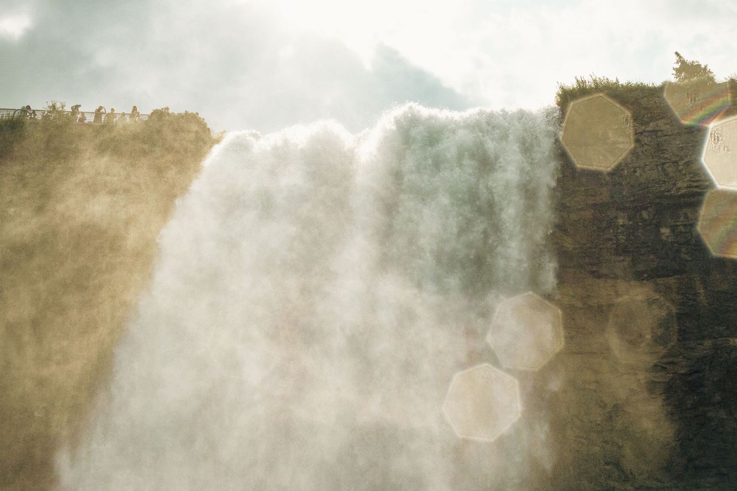 Majestic waterfall cascading over rocky cliffs with golden sunlight and mist creating bokeh light effects.