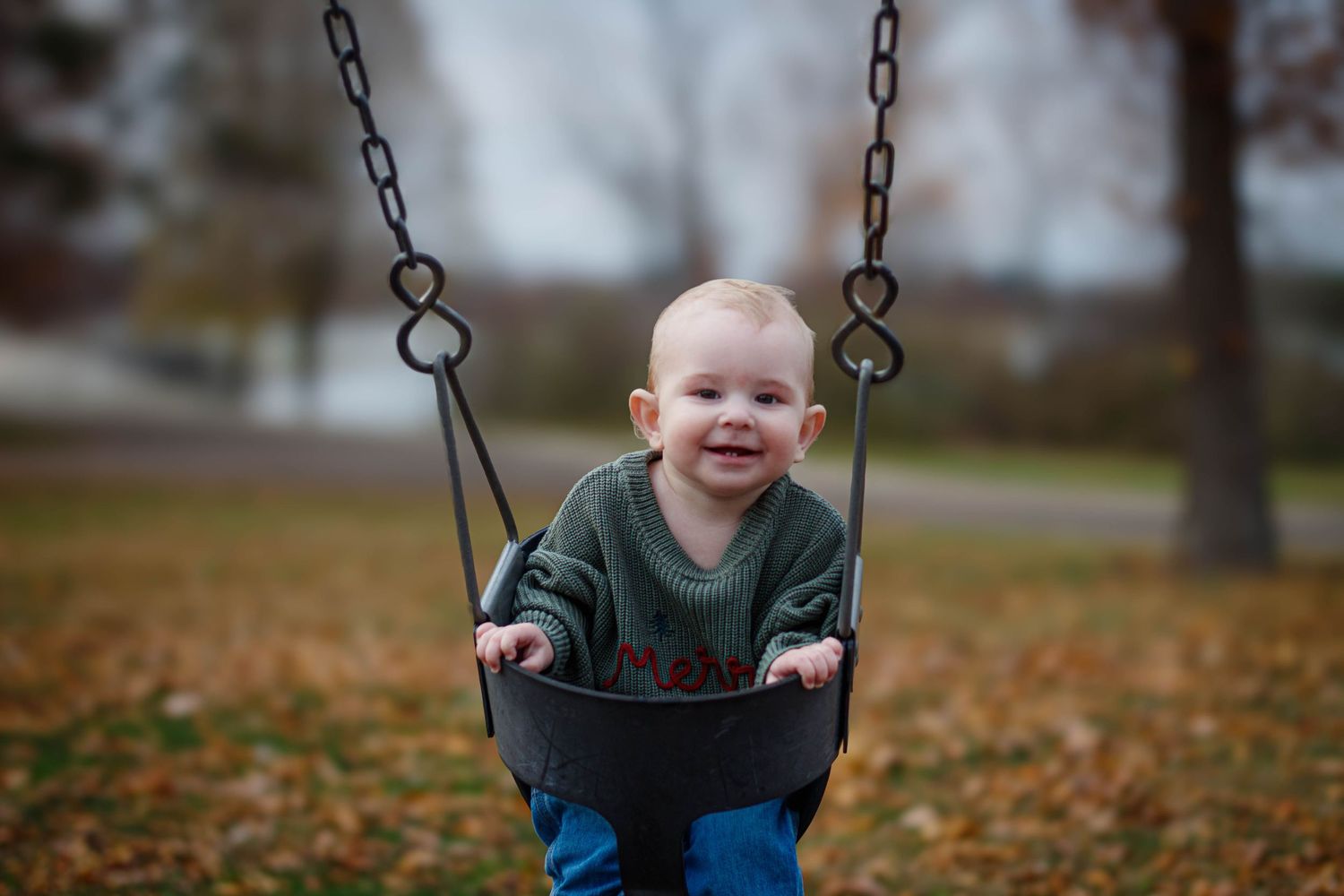 Child laughing joyfully while swinging at a playground on an autumn day.