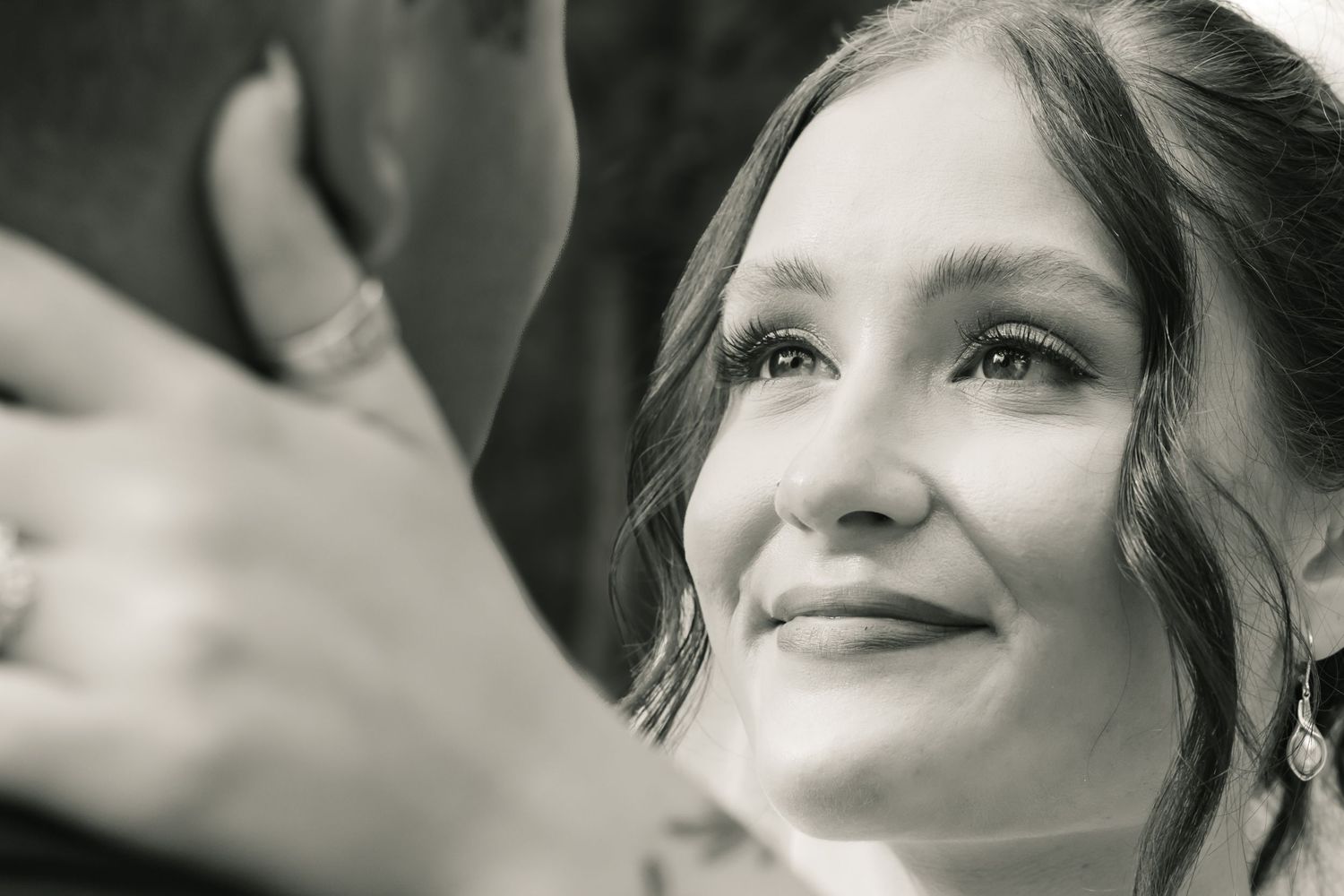 Black and white wedding photo of a tearful smiling bride gazing lovingly at groom, capturing an emotional ceremony moment.