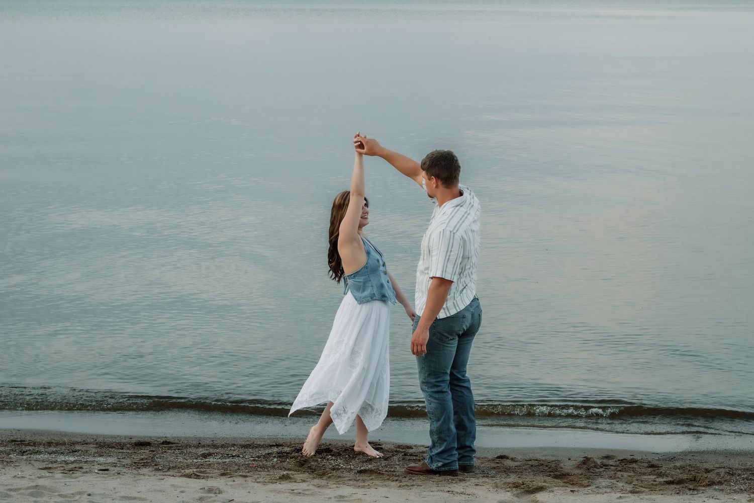 Couple dancing romantically on a sandy beach at sunset near calm ocean waters.