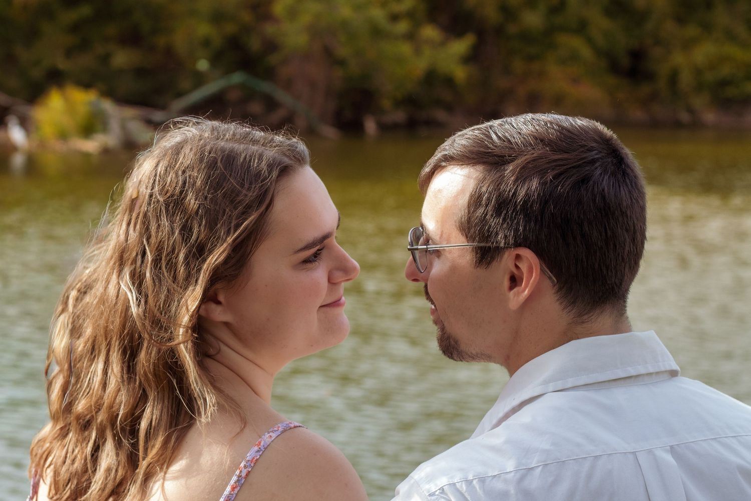 Couple shares an intimate moment by a waterfront during an autumn photoshoot.
